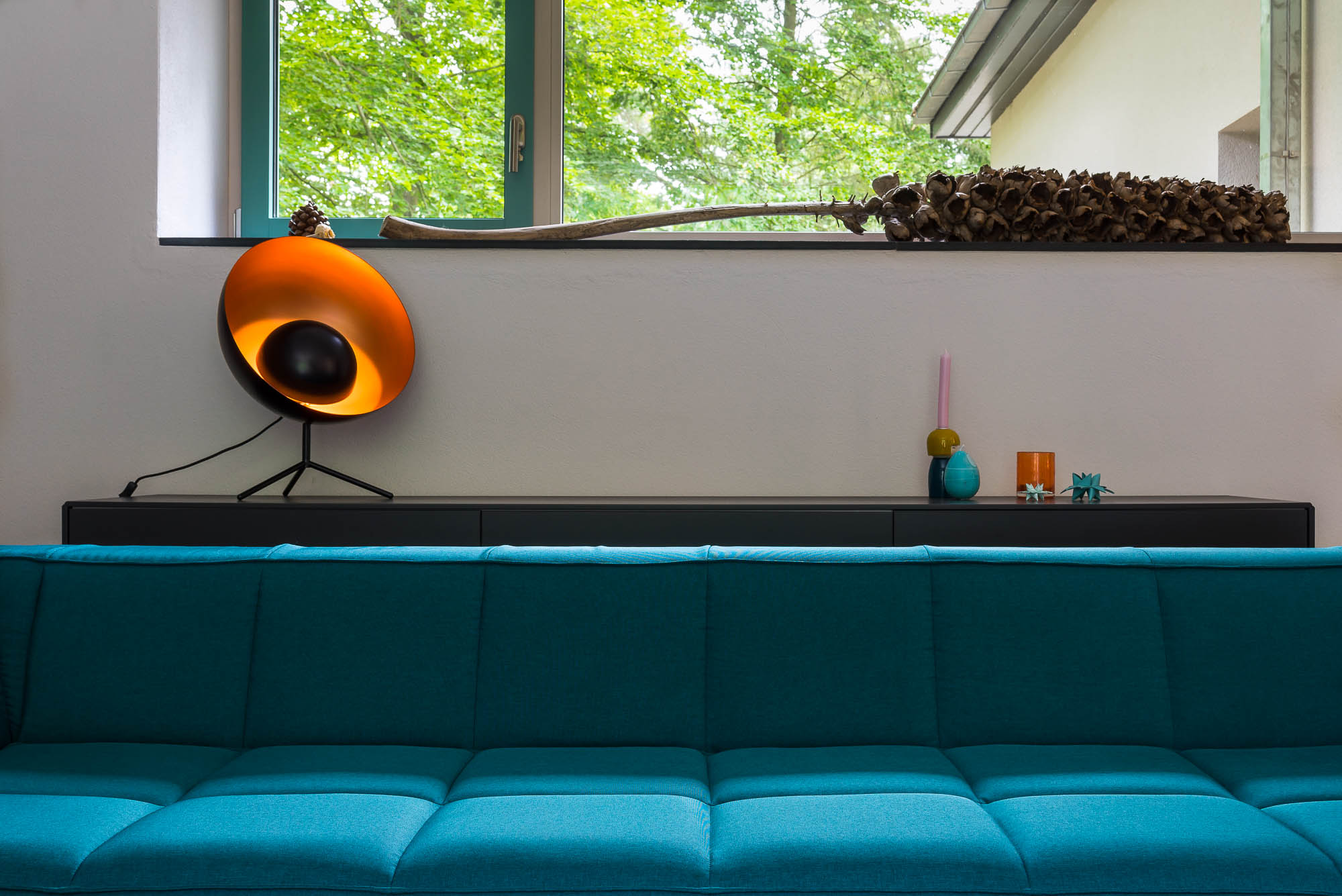 Tageslicht-Wohnbereich mit türkisfarbenem Sofa und Fensterblick