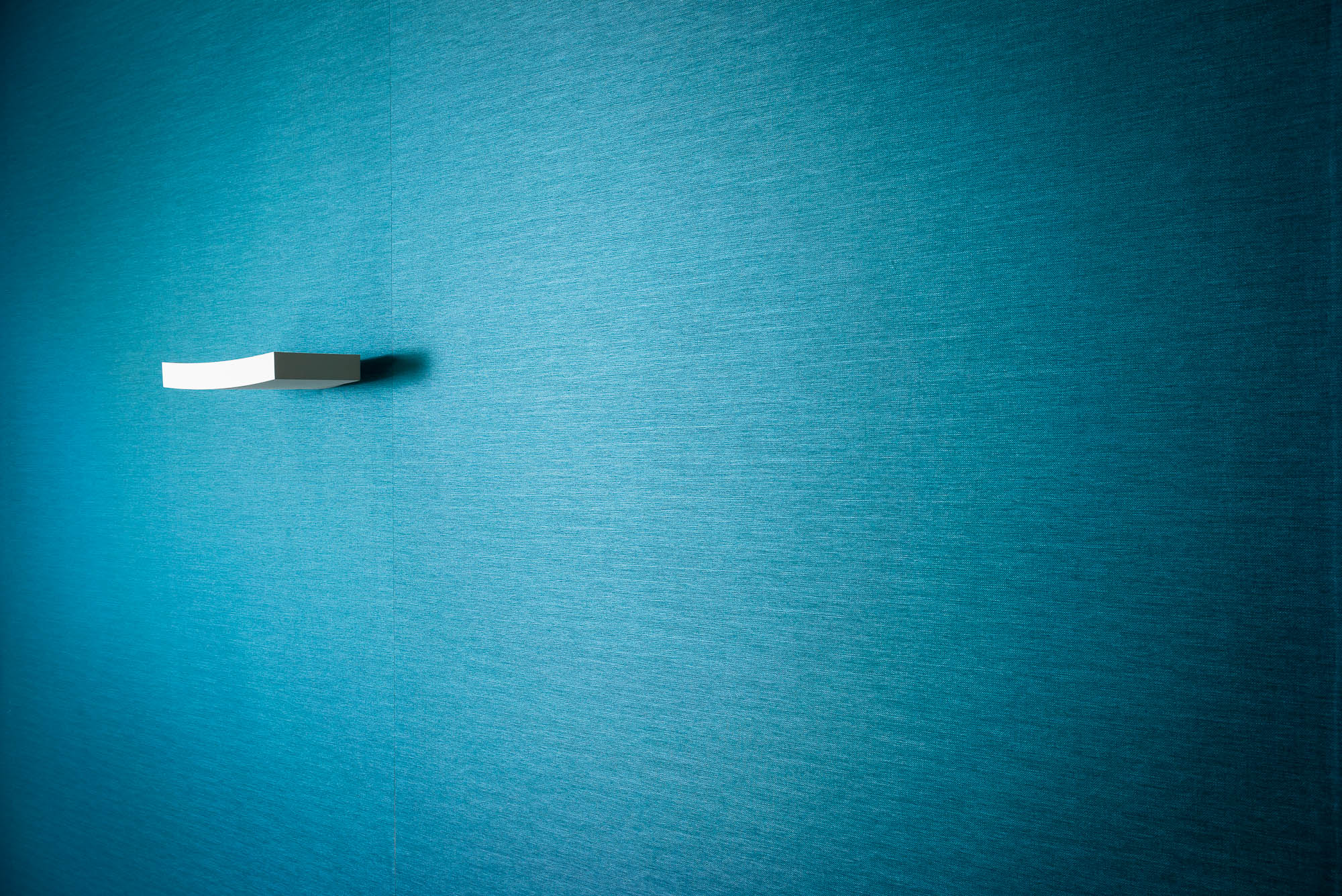 Detailaufnahme einer blauen Wand mit minimalistischer Leuchte