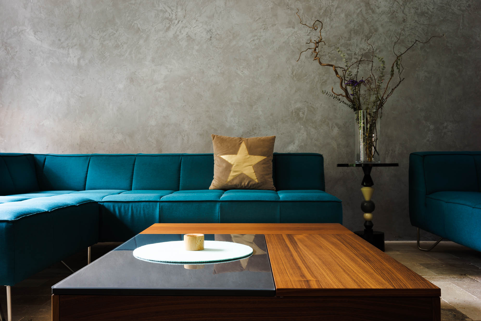 Wohnzimmer mit grauer Wand, Holztisch und türkisem Sofa
