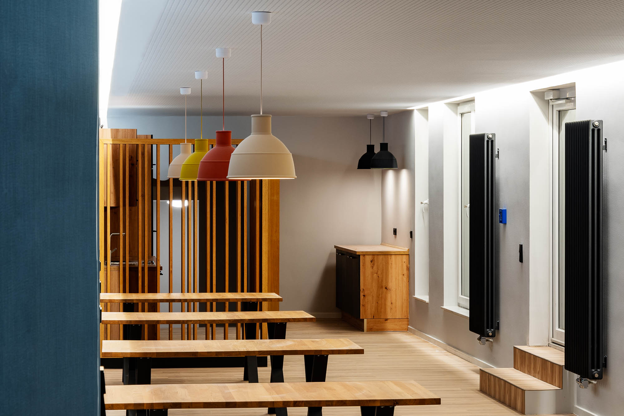 Aufenthaltsraum mit Holztischen, Pendelleuchten und Holzlamellenwand in der Ärztekammer Rostock