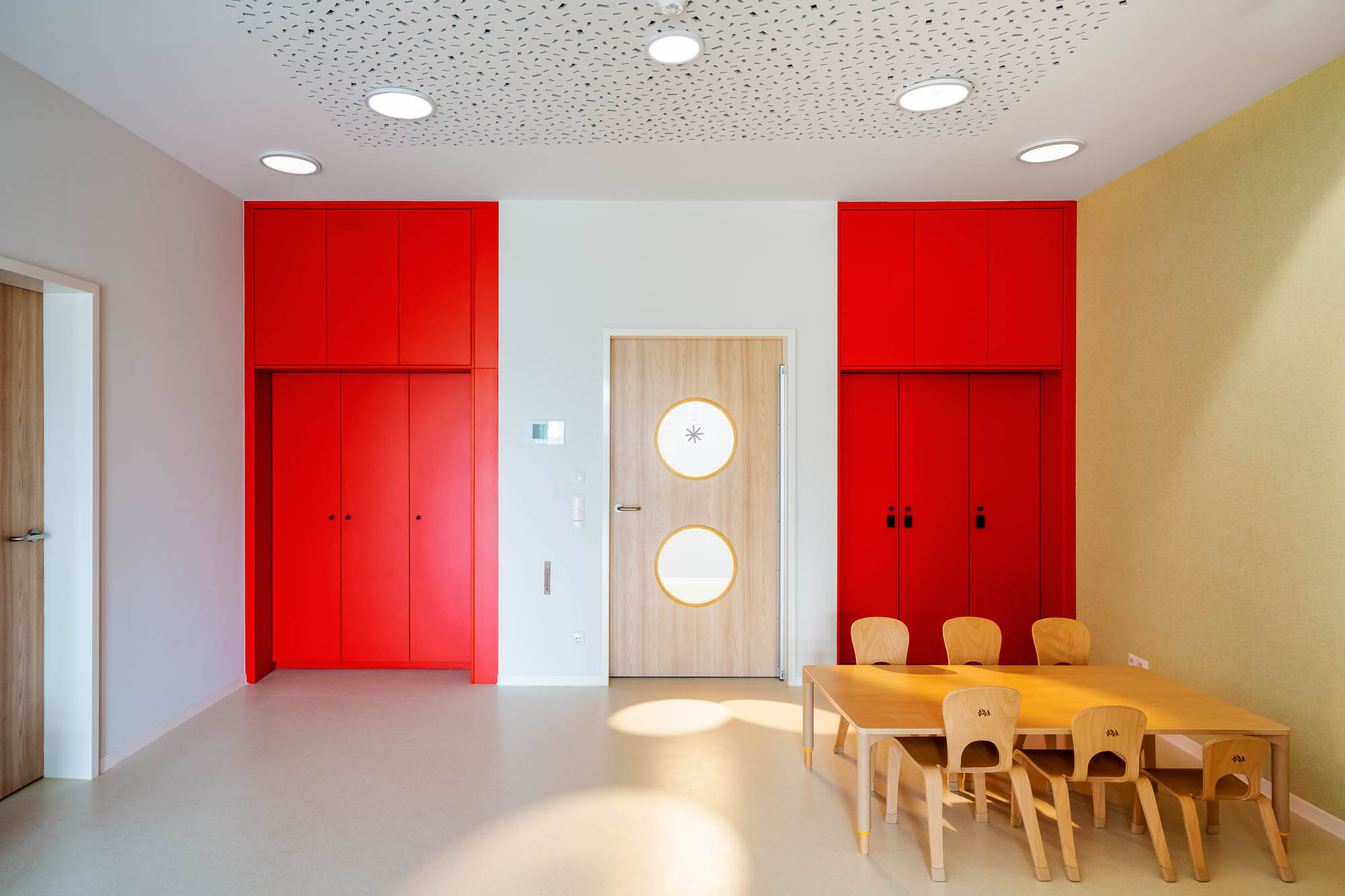 Gruppenraum der Kita mit roter Wand und Kindertischen